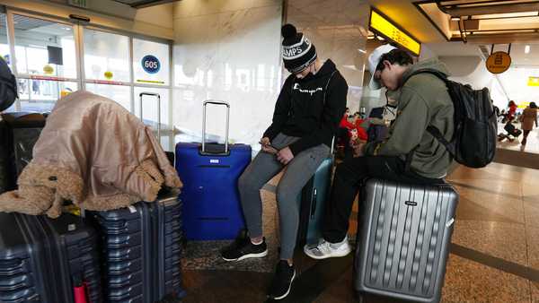 Travelers use their baggage for seats near the Southwest Airlines baggage carousels in Denver International Airport, Sunday, Dec. 26, 2021, in Denver. Airlines canceled hundreds of flights Sunday, citing staffing problems tied to COVID-19 to extend the nation's travel problems beyond Christmas. (AP Photo/David Zalubowski)