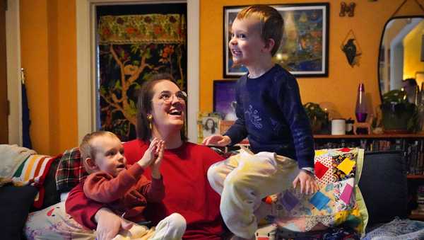Heather Cimellaro holds her three-year-old son Charlie while his twin brother, Milo, jumps on a couch at their home, Wednesday, Jan. 5, 2022, in Auburn, Maine. Heather Cimellaro is one of many parents concerned about the omicron surge and the dilemma it's posing for families of children too young to be vaccinated. (AP Photo/Robert F. Bukaty)