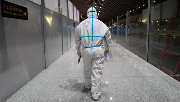 FILE - A member of airport personnel dressed in protective gear leads passengers into the customs area at the Beijing Capital International Airport ahead of the 2022 Winter Olympics in Beijing, Jan. 24, 2022. (AP Photo/Jae C. Hong, File)