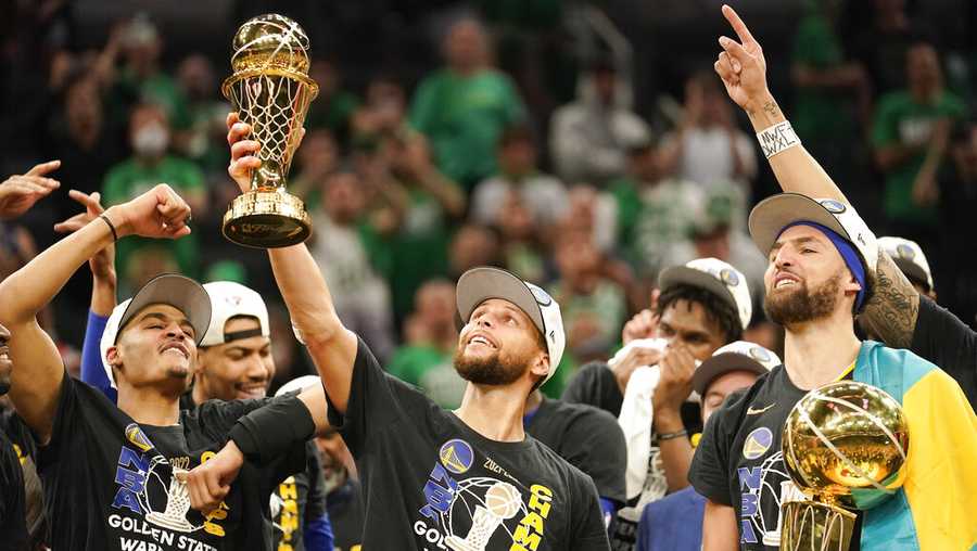 Golden State Warriors guard Stephen Curry, center, holds up the Bill Russell Trophy for most valuable player after the Warriors defeated the Boston Celtics in Game 6 to win basketball&apos;s NBA Finals championship, Thursday, June 16, 2022, in Boston. (AP Photo/Steven Senne)