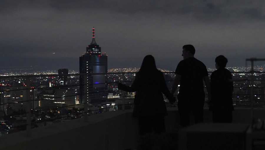 A family looks out at Mexico City from their apartment building rooftop after an earthquake early Thursday, Sept. 22, 2022. The magnitude 6.8 quake struck at 1:19 a.m. local time, causing at least two deaths, damaging buildings and setting off landslides near the epicenter in the western state of Michoacan. (AP Photo/Marco Ugarte)