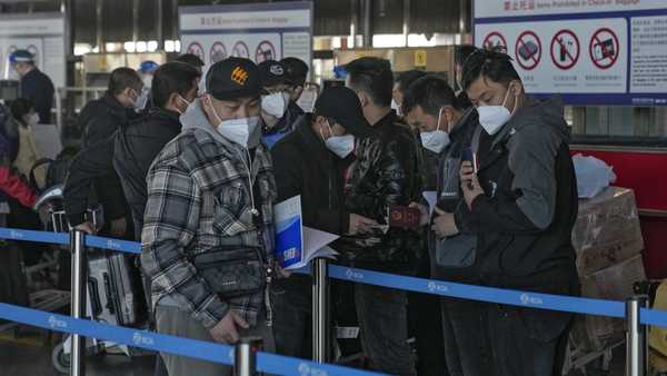 Masked travelers check their passports as they line up at the international flight check in counter at the Beijing Capital International Airport in Beijing, Thursday, Dec. 29, 2022.