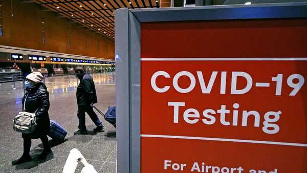 FILE - Travelers pass a sign near a COVID-19 testing site in Terminal E at Logan Airport, on Dec. 21, 2021, in Boston. The nation's top public health agency is expanding a program that tests international travelers for COVID-19 and other infectious diseases. The Centers for Disease Control and Prevention currently operates a program at six U.S. airports that asks passengers from inbound international flights to agree to nose swabs and answer questions about their travel. (AP Photo/Charles Krupa, File)