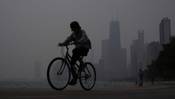 A person rides a bicycle along the shore of Lake Michigan as the downtown skyline is blanketed in the haze from Canadian wildfires on June 27, 2023, in Chicago. Forecasters say there won't be large breaks for much of America anytime soon from eye-watering dangerous smoke from fire-struck Canada. (AP Photo/Kiichiro Sato, File)