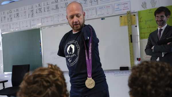 Archer Matt Stutzman of United States shows his silver medal from the Paralympic Games in 2012 to pupils, in a Paris school, in Paris, Wednesday, Oct. 4, 2023. Visiting France's capital before Paralympic tickets go on sale next week, Stutzman dropped by a Paris school on Wednesday and wowed its young pupils with his shooting skills.