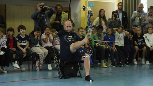 Archer Matt Stutzman of United States holds the bow with his foot during a performance in a Paris school, in Paris, Wednesday, Oct. 4, 2023. Visiting France's capital before Paralympic tickets go on sale next week, Stutzman dropped by a Paris school on Wednesday and wowed its young pupils with his shooting skills. (AP Photo/Thibault Camus)