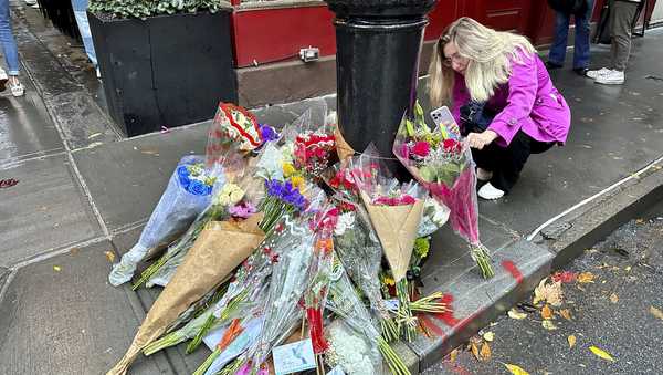 A person takes pictures of a makeshift memorial for Matthew Perry outside the building known as the "Friends" building in New York, Sunday, Oct. 29, 2023. Fans lingered in the rain, taking pictures and leaving flowers on the corner outside the building shown in exterior shots on the popular TV show. Perry, who played Chandler Bing on NBC's 