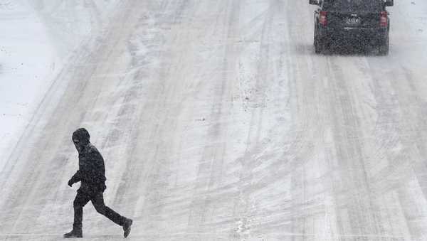 A pedestrian makes his way across a snow covered street, Thursday, Jan. 18, 2024, in downtown Des Moines, Iowa. (AP Photo/Charlie Neibergall)