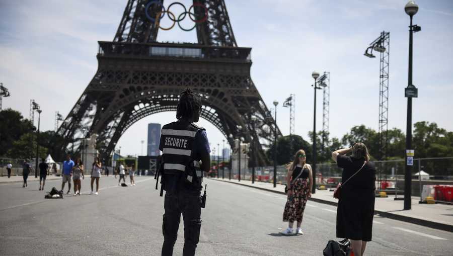 A security officer watches people taking photographs in front of the Eiffel Tower ahead of the 2024 Summer Olympics, Saturday, July 20, 2024, in Paris, France. Three days before the start of the Olympics, France&apos;s Interior Minister has hailed the country’s law enforcement for their hard work in making the Paris Games safe for 10,500 athletes and millions of visitors. (AP Photo/Thomas Padilla, File)