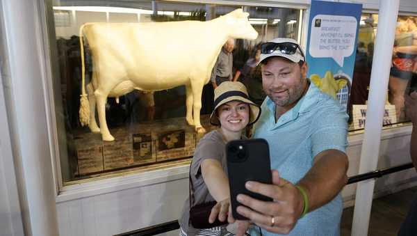 Melissa Bohnker and her husband Seth, of Matawan, N.J., pose for a selfie photo in front of the butter cow at the Iowa State Fair, Friday, Aug. 11, 2023, in Des Moines, Iowa. (AP Photo/Charlie Neibergall)