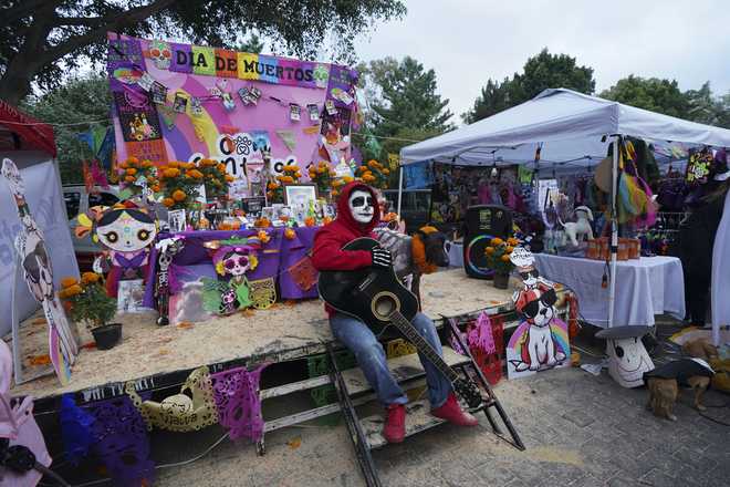 El dueño de una mascota posa con su perro frente a un altar del Día de Muertos que conmemora a los muertos, el domingo 27 de octubre de 2024, en la Ciudad de México. (Foto AP/Fabiola Sánchez)