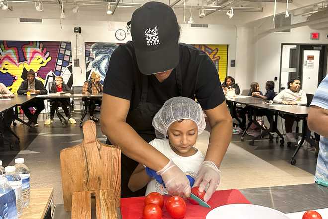 La chef Sharri Eiji ayuda a Yareni Orduna-Herrera a cortar tomates para hacer una pizza margherita como parte del Snack Hack de la Biblioteca Pública de Milwaukee, un programa de comidas extraescolares que enseña a los niños a cocinar comidas saludables en casa, el 19 de noviembre de 2024, en Milwaukee. (Foto AP/Devi Shastri)