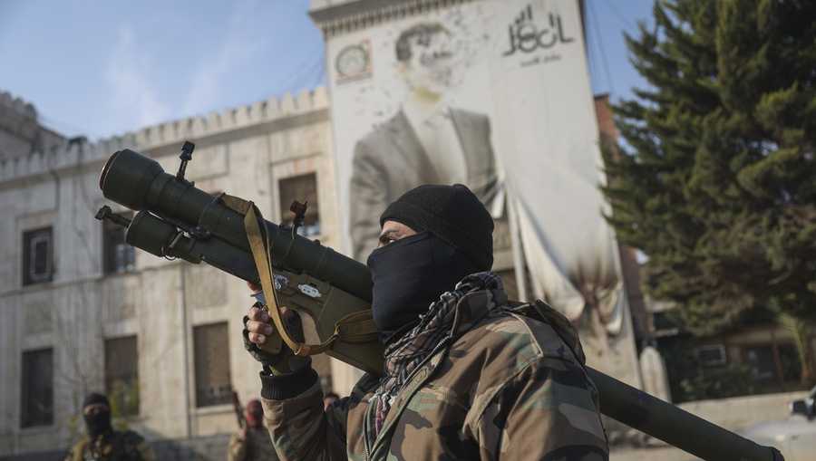 A Syrian opposition fighter holds a rocket launcher in front of the provincial government office, where an image of Syrian President Bashar Assad is riddled with bullets on the facade, in the aftermath of the opposition&apos;s takeover of Hama, Syria, Friday, Dec. 6, 2024. (AP Photo/Ghaith Alsayed)