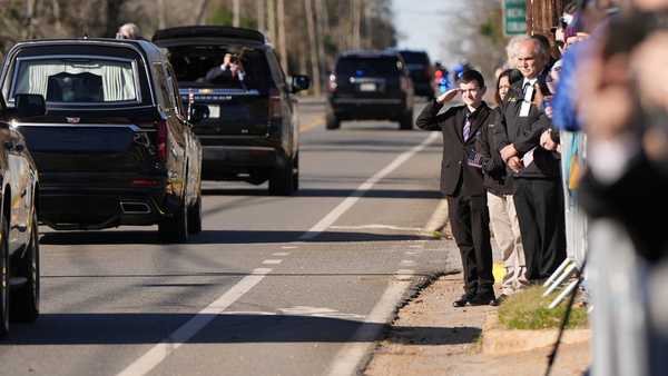 A young boy salutes as the hearse carrying the flag-draped casket of former President Jimmy Carter moves through downtown Plains, Ga., Saturday, Jan. 4, 2025. (AP Photo/Mike Stewart)