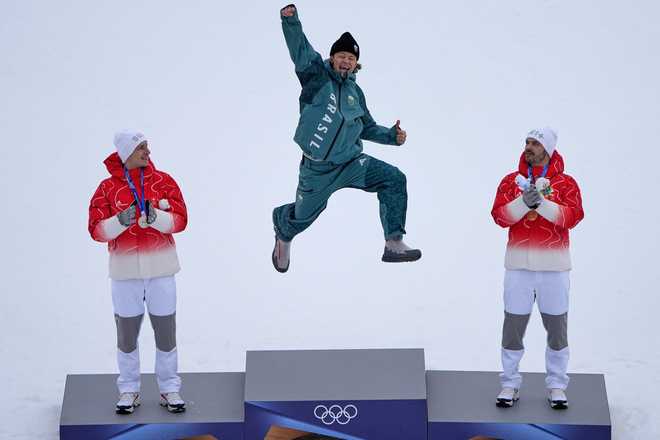 Brazil's Lucas Pinheiro Braathen, center, winner of an alpine ski, men's giant slalom race, jumps in celebration on the podium flanked by second-place Switzerland's Marco Odermatt, left, and third-place Switzerland's Loic Meillard, at the 2026 Winter Olympics, in Bormio, Italy, Feb. 14, 2026.