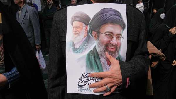 A mourner holds a poster depicting Ayatollah Mojtaba Khamenei, right, the successor to his late father Ayatollah Ali Khamenei, left, as supreme leader, during the funeral procession for senior Iranian military officials and civilians killed during the U.S.-Israel campaign in Tehran, Iran, Wednesday, March 11, 2026. (AP Photo/Vahid Salemi)