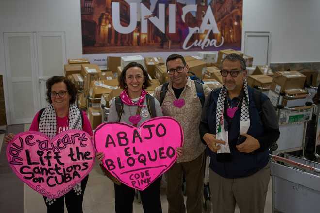 CODEPINK activists hold signs in front of boxes of aid they brought as part of the &amp;quot;Nuestra America,&amp;quot; or Our America Convoy, after landing at the airport in Havana, Cuba, Friday, March 20, 2026. (AP Photo/Ramon Espinosa)