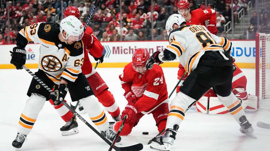 Detroit Red Wings center Pius Suter (24) battles with Boston Bruins left wing Brad Marchand (63) and Dmitry Orlov (81) for the puck in the second period of an NHL hockey game Sunday, March 12, 2023, in Detroit.