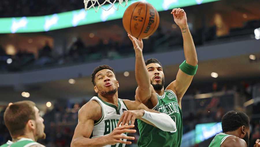 Boston Celtics forward Jayson Tatum, center, reaches for a rebound against Milwaukee Bucks forward Giannis Antetokounmpo (34) after chipping the tooth of guard Jaylen Brown, right, during the first half of an NBA basketball game Saturday, Dec. 25, 2021, in Milwaukee.