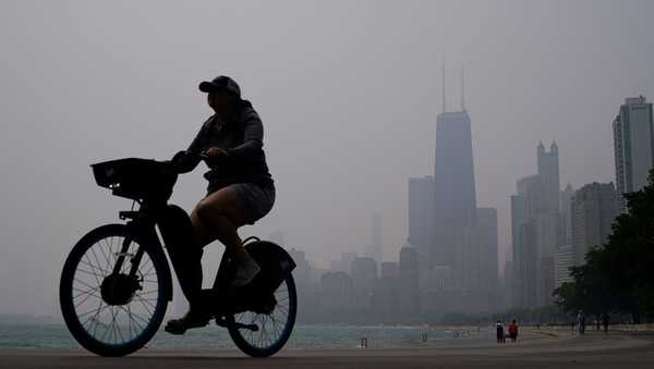 A person rides a bicycle along the shore of Lake Michigan as the downtown skyline is blanketed in haze from Canadian wildfires on June 27 in Chicago.