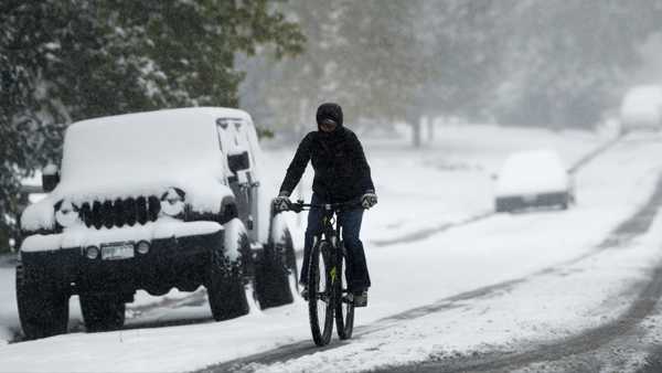 A bicyclist uses a tire track to guide her bicycle down South Monroe Street as the season's first snow storm sweeps over the metropolitan area Thursday, Oct. 10, 2019, in Denver. Forecasters predict that the snow will move out and cold temperatures will envelope the area as the storm moves on to the plains. (AP Photo/David Zalubowski)