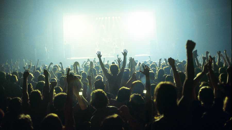 A general view of a rock concert taken from the back for a venue showing the audience in silhouette raising their arms and cheering with bright lights shining from the stage, circa 1980.
