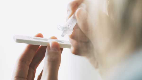 Close up of woman placing liquid drops into antigen test strip