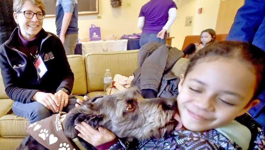 Leila Martinez, 8, of New Haven, right, gets a kiss from certified therapy dog Sophia, a rescued mixed-breed, on Saturday with her handler Roben River, of Woodbridge, representing dog training facility Paw’s N’ Effect of Hamden.