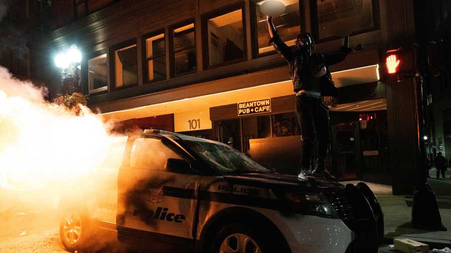 A protestor stands on top of a burning Boston police car Sunday night.