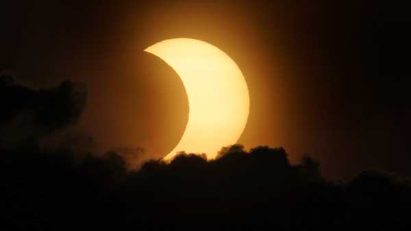 A partially eclipsed sun peaks out from behind a cloud as it rises over lower Manhattan in New York, Thursday, June 10, 2021.