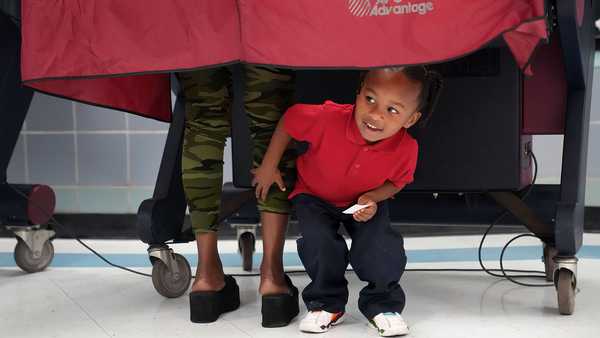 Kash Strong, 3, peeks out from under the curtain of a voting booth as his mother Sophia Amacker casts her vote on Election Day at the Martin Luther King Elementary School in the Lower Ninth Ward of New Orleans, Tuesday, Nov. 8, 2022.