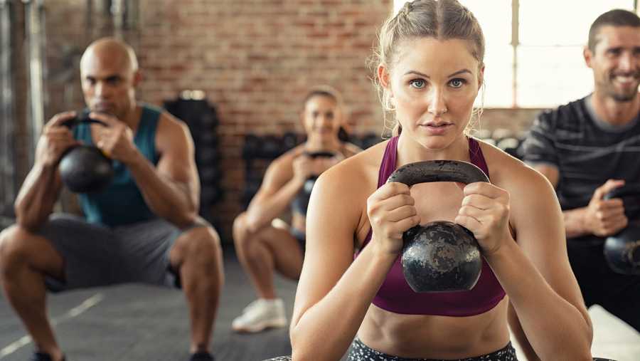 people hold kettle bells during a squatting exercise at a gym