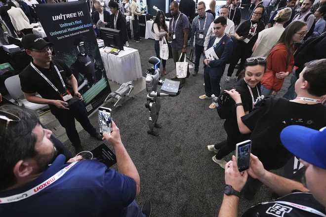 A human-like Unitree robot is surrounded by convention guests while passing out company brochures at the Robotics Summit &amp; Expo, Wednesday, April 30, 2025, in Boston.
