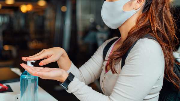A woman is applying hand sanitizer to her hands and fingers before entering a gym.