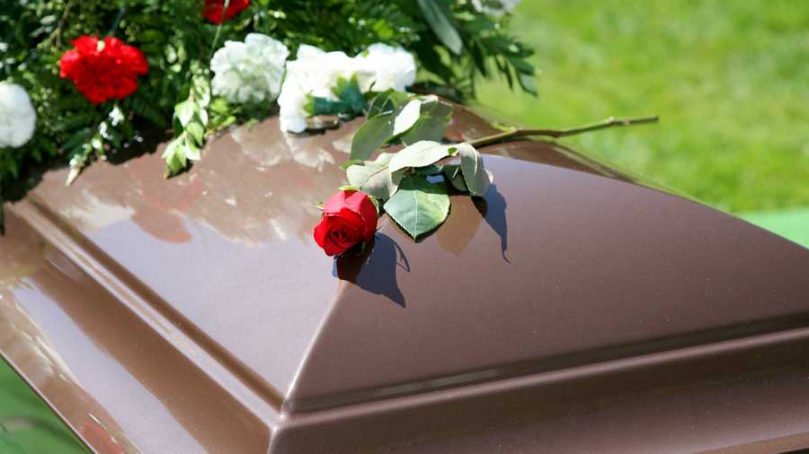 A single brown casket with a spray of flowers.