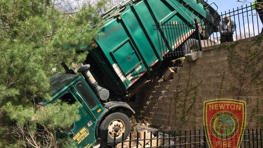 Garbage truck crashes, hangs over retaining wall in Mass.