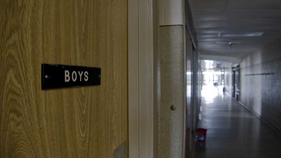 Sign on boys room door in a dark school hall.