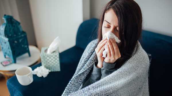 Sick woman blowing her nose, she covered with blanket