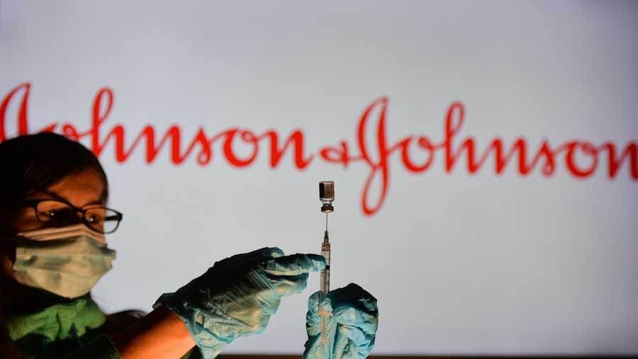 A person holding a medical syringe and a vaccine vial in front of the Johnson and Johnson logo