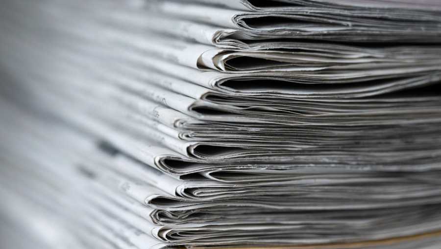 A stack of various daily newspapers lies on a table.