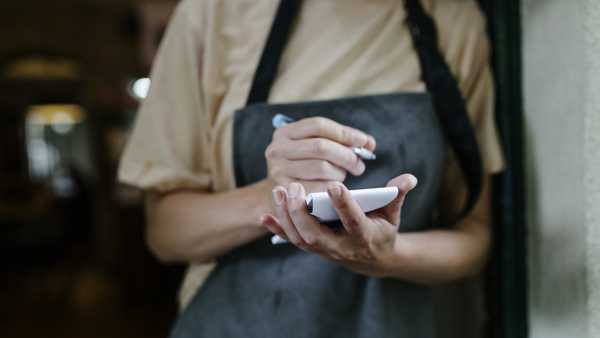 A waitress standing in the doorway of a restaurant and writing on her notepad.
