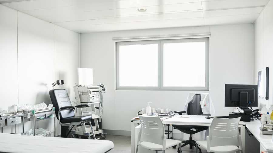 Furniture and medical equipment at doctor&apos;s office. Empty chairs are at desk in clinic during COVID-19. Interior of medical examination room.
