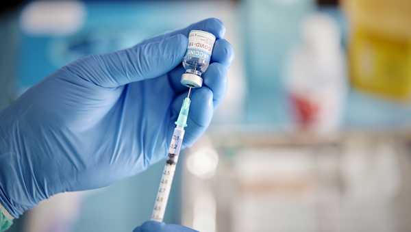 A healthcare Worker hands in surgical gloves pulling COVID-19 vaccine liquid from vial to vaccinate a patient