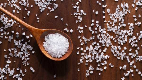 Sea Salt Grains in Wooden Spoon on Brown Wooden Background.