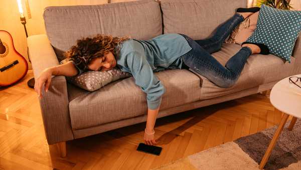 Exhausted young Caucasian woman lying on comfortable sofa in living room sleeping after hard-working day, tired millennial female fall asleep on couch at home.