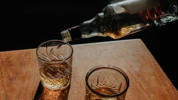 A bottle of whisky is poured into a cut glass tumbler over ice. Space for copy.