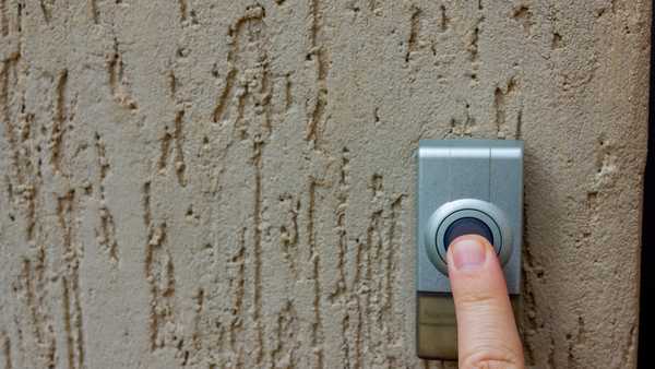 Selective focus on a caucasian finger pressing a  round button on an outdoor doorbell. The doorbell is mounted on a textured wall