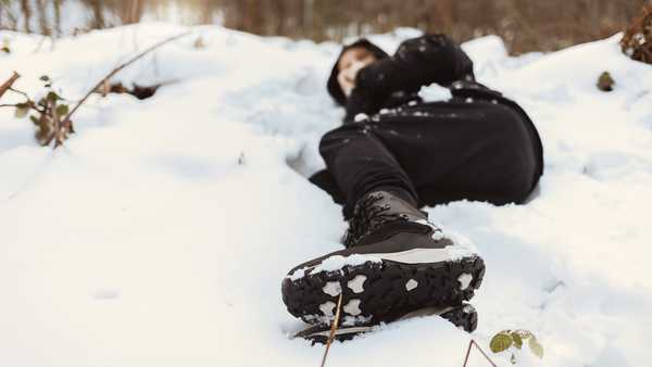 Photo of a men with hypothermia lying down surrounded by frozen winter landscape. Young man blowing in his hands to warm up in the cold winter environment. Cold and loneliness.