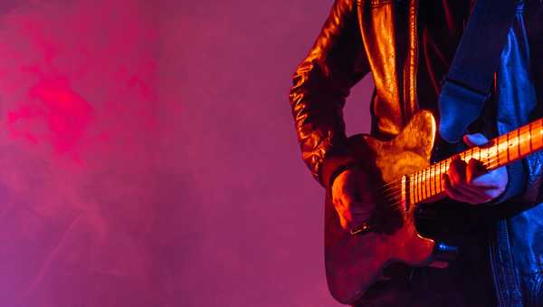 Unrecognizable man guitarist plays music on the guitar on a colored background.