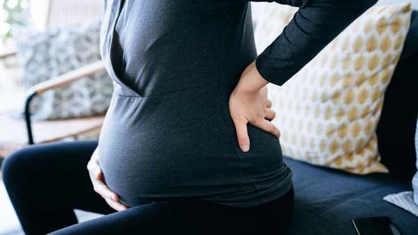 Mid-section of pregnant woman touching her baby bump and lower back